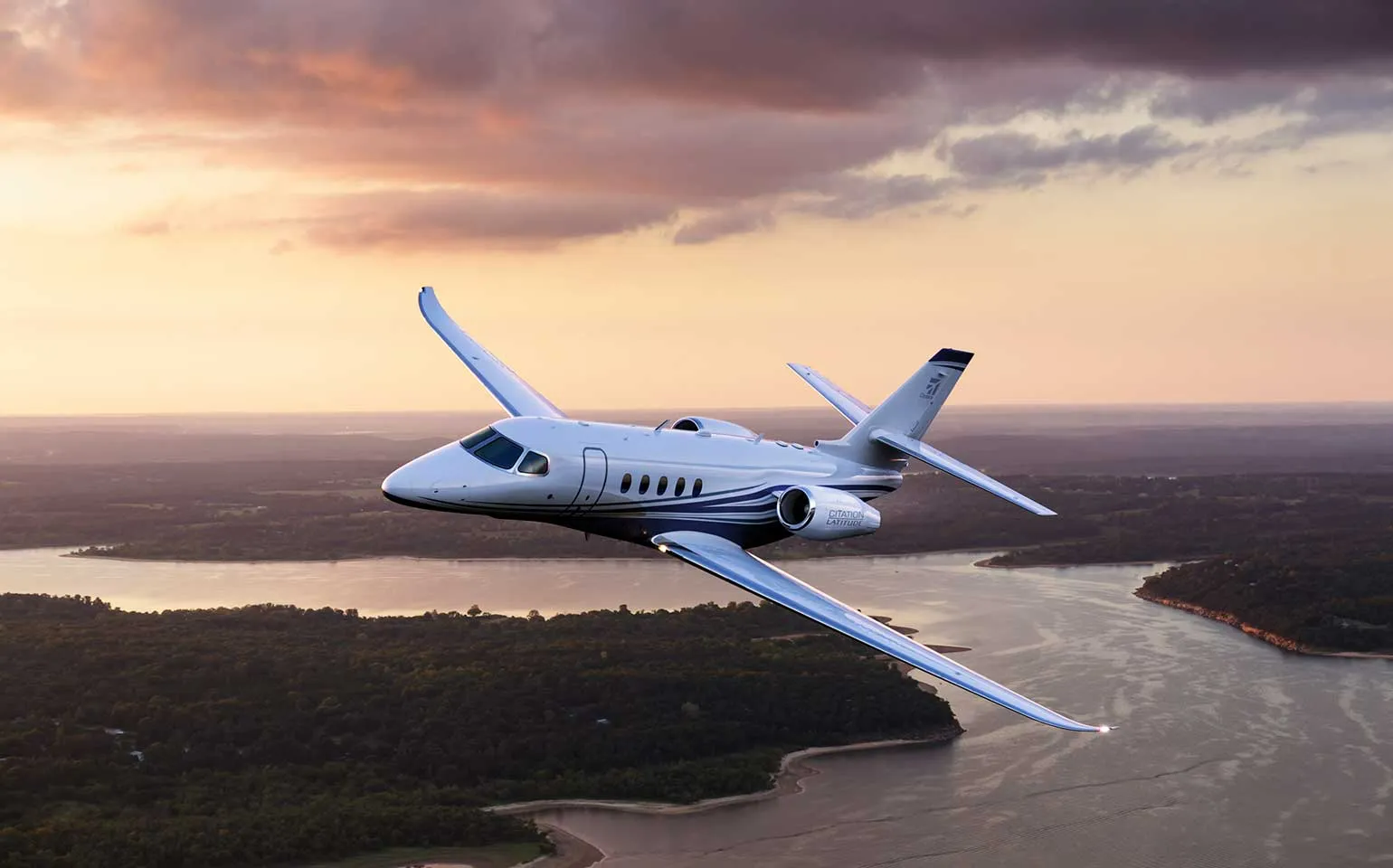 Citation Latitude jet flying over river at sunset