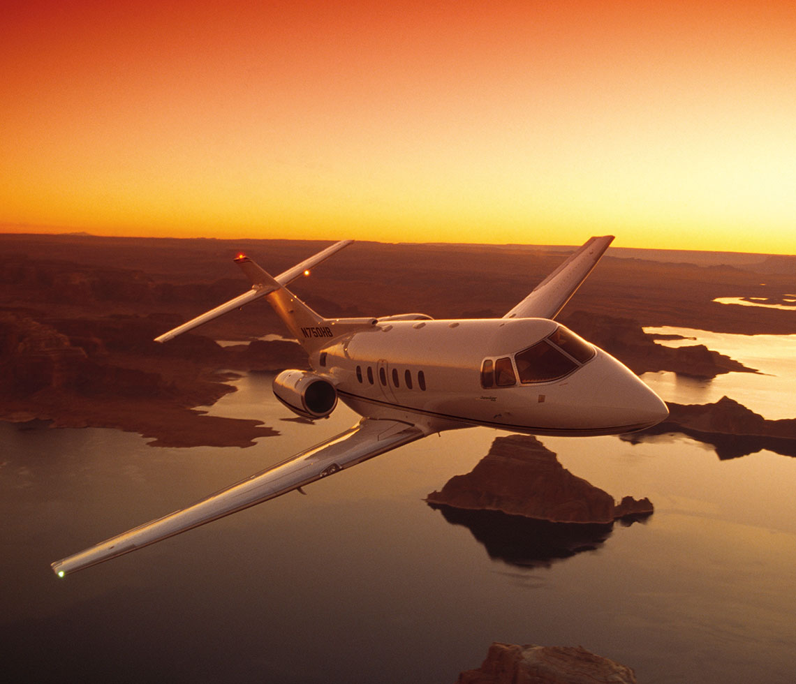 Hawker 750 private jet charter flying over canyon during golden sunset